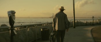 Movie still from “Blaze” (2018), directed by Ethan Hawke – An older man walking down a sidewalk near the water; Wide shot, Low angle