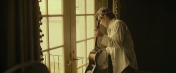 Movie still from “Blaze” (2018), directed by Ethan Hawke – A man standing in front of an open window holding a guitar; Medium shot, Low angle