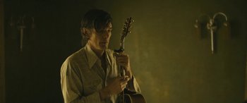 Movie still from “Blaze” (2018), directed by Ethan Hawke – A man holding a guitar in a dark room; Medium shot, Low angle