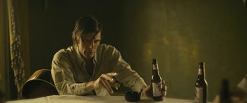 Movie still from “Blaze” (2018), directed by Ethan Hawke – A man sitting at a table with a bottle of beer and a cigarette; Medium shot, High angle