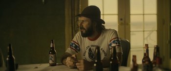 Movie still from “Blaze” (2018), directed by Ethan Hawke – A man sitting at a table in front of two beer bottles; Medium shot, Over the shoulder angle