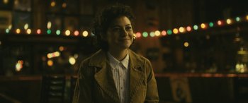 Movie still from “Blaze” (2018), directed by Ethan Hawke – A woman wearing a brown jacket standing in front of lights at night; Close Up shot, Over the shoulder angle