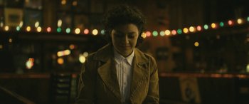 Movie still from “Blaze” (2018), directed by Ethan Hawke – A woman wearing a brown jacket standing next to a wall; Close Up shot, High angle