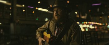 Movie still from “Blaze” (2018), directed by Ethan Hawke – A man with a beard wearing a hat and holding a guitar; Close Up shot, Low angle