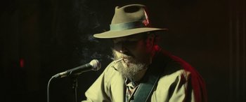 Movie still from “Blaze” (2018), directed by Ethan Hawke – A man with a beard wearing a hat smoking a cigarette; Close Up shot, Over the shoulder angle