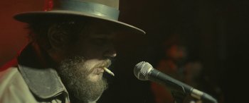 Movie still from “Blaze” (2018), directed by Ethan Hawke – A man with a beard wearing a hat and smoking a cigarette; Close Up shot, Over the shoulder angle