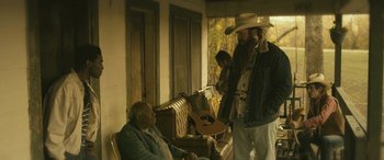 Movie still from “Blaze” (2018), directed by Ethan Hawke – A man standing next to another man holding a guitar; Medium shot, Over the shoulder angle