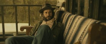 Movie still from “Blaze” (2018), directed by Ethan Hawke – A man sitting on top of a chair wearing a hat; Medium shot, Over the shoulder angle