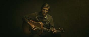 Movie still from “Blaze” (2018), directed by Ethan Hawke – A man sitting down with a guitar in his hands; Medium shot, Over the shoulder angle