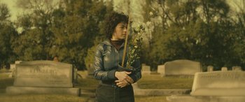 Movie still from “Blaze” (2018), directed by Ethan Hawke – A woman holding a plant in a cemetery; Medium shot, Low angle