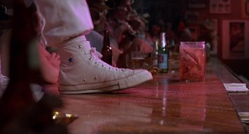 Movie still from “Blood Simple” (1984), directed by Joel Coen – A person standing next to a table with a bottle of beer; Close Up shot, Low angle