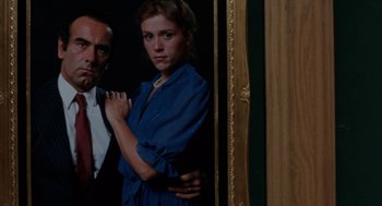 Movie still from “Blood Simple” (1984), directed by Joel Coen – A woman standing in front of a man in a suit and tie; Medium shot, Low angle