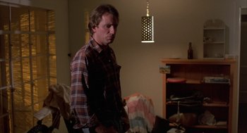 Movie still from “Blood Simple” (1984), directed by Joel Coen – A man standing in a living room in a plaid shirt; Medium shot, Low angle