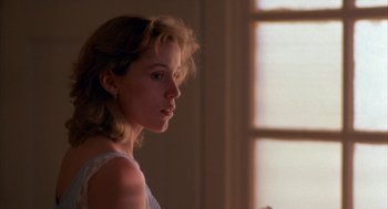 A woman in a white dress looking out of a window
