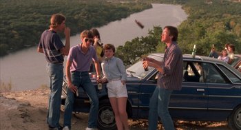 Movie still from “Blood Simple” (1984), directed by Joel Coen – A group of people standing next to a car; Wide shot, High angle