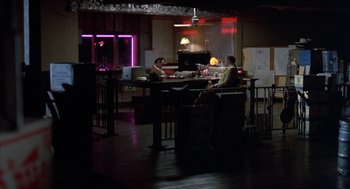 Movie still from “Blood Simple” (1984), directed by Joel Coen – Two people sitting at a table in a dark room; Extreme Wide shot, High angle