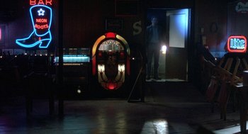Movie still from “Blood Simple” (1984), directed by Joel Coen – A man standing in front of an old jukebox in a dark room; Wide shot, Low angle