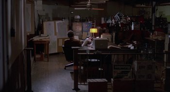 Movie still from “Blood Simple” (1984), directed by Joel Coen – A man sitting at a desk in front of a computer; Wide shot, High angle