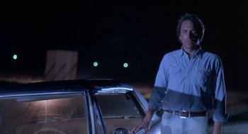 Movie still from “Blood Simple” (1984), directed by Joel Coen – A man standing in front of a car at night; Medium shot, Low angle