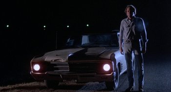 Movie still from “Blood Simple” (1984), directed by Joel Coen – A man standing in front of an old white car at night; Wide shot, Low angle