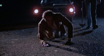 Movie still from “Blood Simple” (1984), directed by Joel Coen – A man is laying on the ground in the dark; Wide shot, High angle