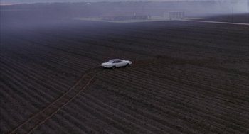 Movie still from “Blood Simple” (1984), directed by Joel Coen – A white car is parked in the middle of a field; Extreme Wide shot, High angle