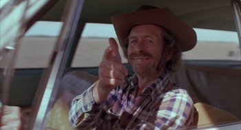 Movie still from “Blood Simple” (1984), directed by Joel Coen – A man in a cowboy hat is smiling and pointing to the camera; Close Up shot, Low angle