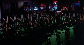 Movie still from “Blood Simple” (1984), directed by Joel Coen – A room filled with neon signs and chairs in the middle of the room; Wide shot, High angle