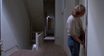Movie still from “Blood Simple” (1984), directed by Joel Coen – A woman standing in a room next to a staircase; Wide shot, Over the shoulder angle