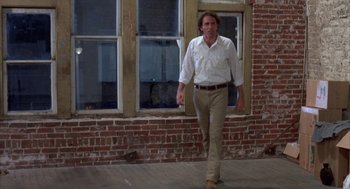 Movie still from “Blood Simple” (1984), directed by Joel Coen – A man walking in front of a brick building; Wide shot, Low angle