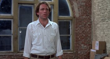Movie still from “Blood Simple” (1984), directed by Joel Coen – A man standing in front of a brick building; Medium shot, Low angle