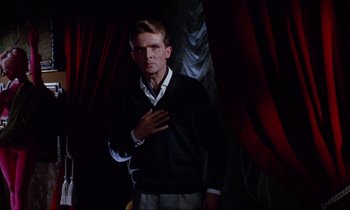 Movie still from “Blood and Black Lace” (1964), directed by Mario Bava – A man standing in front of a curtain with his hand over his heart; Medium shot, Low angle