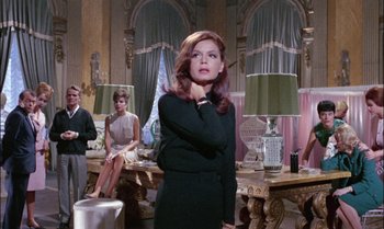 Movie still from “Blood and Black Lace” (1964), directed by Mario Bava – A woman standing in front of two other women in a living room; Medium shot, Low angle