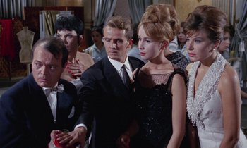 Movie still from “Blood and Black Lace” (1964), directed by Mario Bava – A man and a woman standing next to each other in a crowd; Medium shot, Low angle