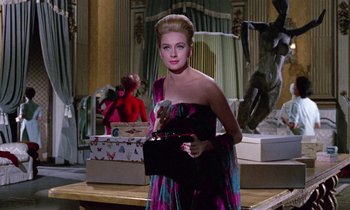 Movie still from “Blood and Black Lace” (1964), directed by Mario Bava – A woman in a colorful dress holding a black purse; Medium shot, Low angle