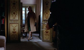 Movie still from “Blood and Black Lace” (1964), directed by Mario Bava – A woman in a coat and gloves walking through a hallway; Wide shot, Over the shoulder angle