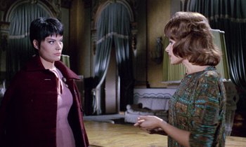Movie still from “Blood and Black Lace” (1964), directed by Mario Bava – Two women are standing in a room and one of them is talking to another woman; Medium shot, Over the shoulder angle