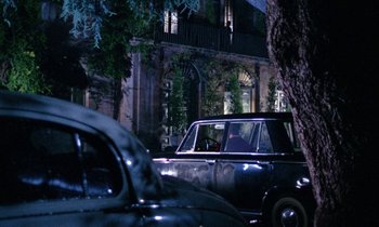 Movie still from “Blood and Black Lace” (1964), directed by Mario Bava – An old car parked in front of a building at night; Wide shot, Over the shoulder angle