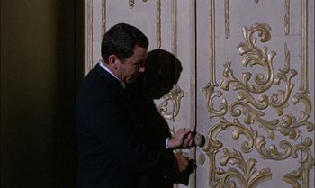 Movie still from “Blood and Black Lace” (1964), directed by Mario Bava – A man in a black suit is looking at his watch; Medium shot, Low angle