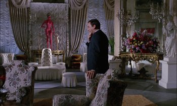 Movie still from “Blood and Black Lace” (1964), directed by Mario Bava – A man standing in a living room talking on a phone; Wide shot, Over the shoulder angle