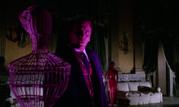 Movie still from “Blood and Black Lace” (1964), directed by Mario Bava – A man in a suit standing in front of a bird cage; Medium shot, Low angle