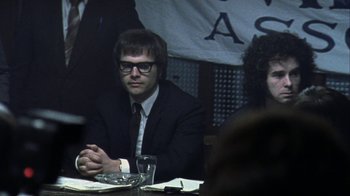 Movie still from “Bloody Sunday” (2002), directed by Paul Greengrass – A man sitting at a table in front of other people; Medium shot, Over the shoulder angle