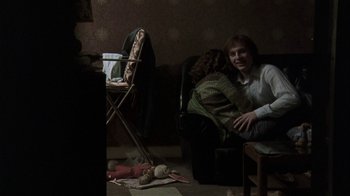 Movie still from “Bloody Sunday” (2002), directed by Paul Greengrass – A man and a woman sitting on a chair in a living room; Wide shot, Over the shoulder angle