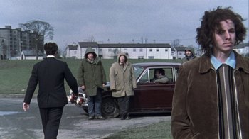 Movie still from “Bloody Sunday” (2002), directed by Paul Greengrass – A group of people standing next to an old car; Wide shot, Over the shoulder angle