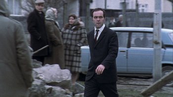 Movie still from “Bloody Sunday” (2002), directed by Paul Greengrass – A man in a suit and tie walking in front of a car; Medium shot, Low angle