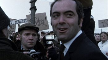 Movie still from “Bloody Sunday” (2002), directed by Paul Greengrass – A man in a suit and tie holding up a camera; Close Up shot, Low angle