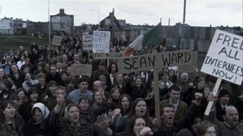 Movie still from “Bloody Sunday” (2002), directed by Paul Greengrass – A crowd of people holding signs in front of a building; Wide shot, High angle