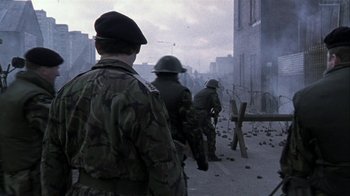 Movie still from “Bloody Sunday” (2002), directed by Paul Greengrass – A group of men standing next to each other on a street; Wide shot, Over the shoulder angle