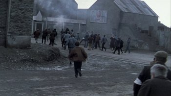Movie still from “Bloody Sunday” (2002), directed by Paul Greengrass – A group of people walking down a street near a building; Extreme Wide shot, High angle