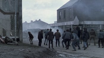 Movie still from “Bloody Sunday” (2002), directed by Paul Greengrass – A group of people walking down a street near buildings; Wide shot, High angle